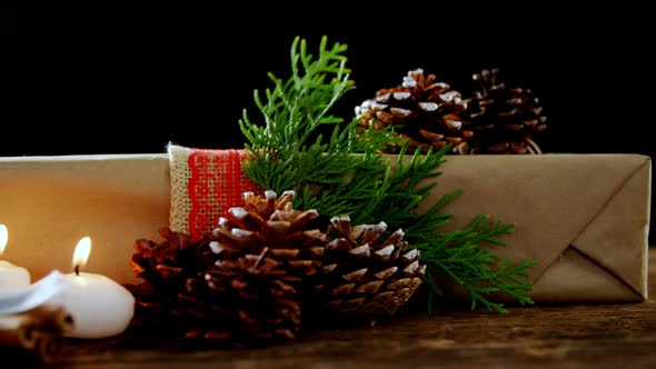 Burning candles, gift box and pine cones against black background alt