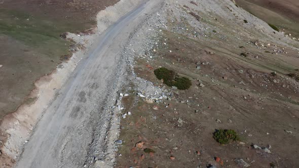 Top View of a Flight Over a Sandy Mountain Road with a Lot of Stones and Green Grass