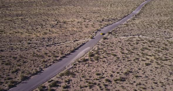 Aerial view of yellow sport car driving on asphalt road in the middle of dusty dry desert land. alt
