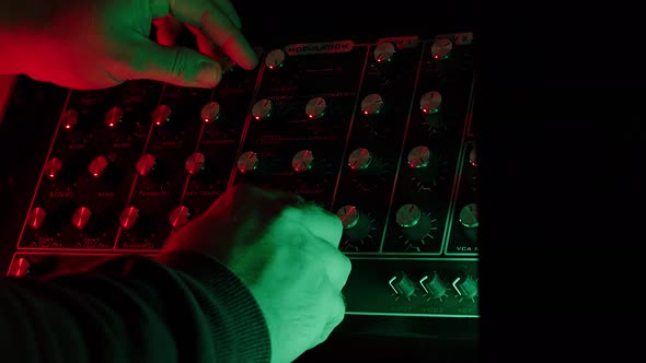 slow motion shot, close up, man turnig knobs on vintage synth during live show, dark mood alt