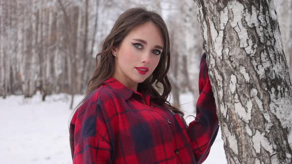 Young Woman with Wavy Hair Standing and Touching Face in Winter Forest