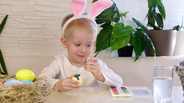 A little boy in rabbit ears paints Easter eggs with paint and smiles. Religious holidays concept
