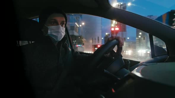 Man in Surgical Face Mask Drives Car at Night. COVID-19 Coronavirus Pandemic