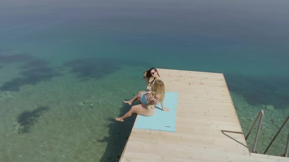 Aerial view of two women sits on wooden deck in Panagopoula, Greece. alt