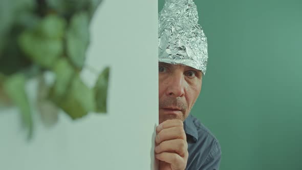 A Frightened Man in a Protective Foil Cap Peeking Strangely Around the Corner alt