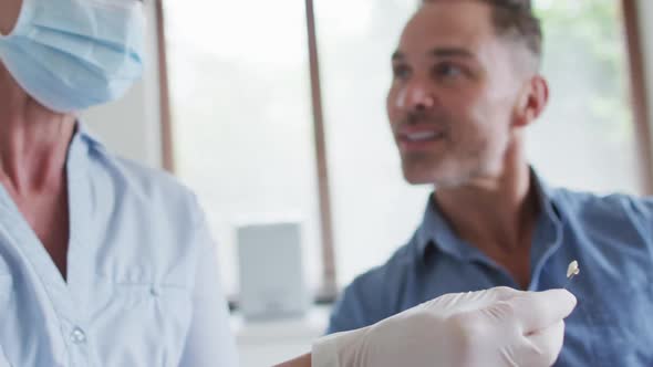 Caucasian female dental nurse with face mask examining teeth male patient at modern dental clinic alt