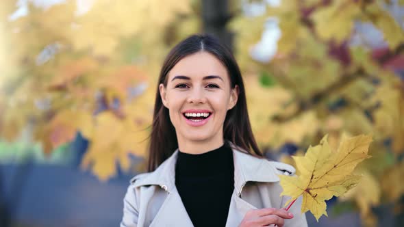 Portrait of Woman Hiding Face Behind Dry Yellow Maple Leaf alt
