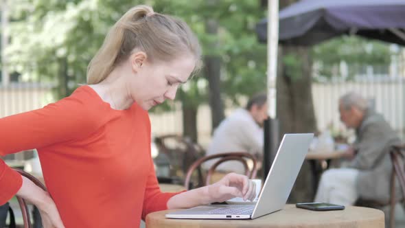 Young Woman Working on Laptop and Drinking Coffee Sitting in Cafe Terrace alt