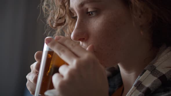 Close up of caucasian red head woman cold and drinking hot tea in the living room. alt