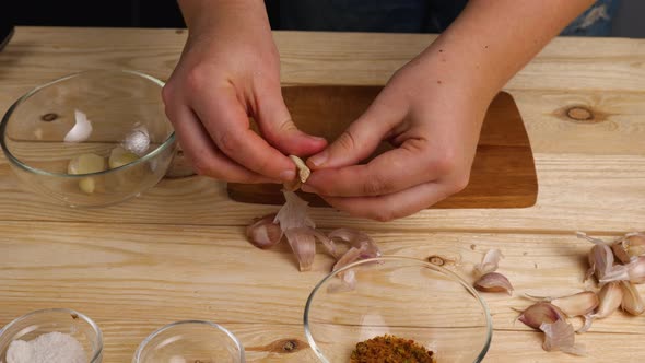 Peeling garlic from husks in the home kitchen. A woman's hands peel garlic and put it in a bowl alt
