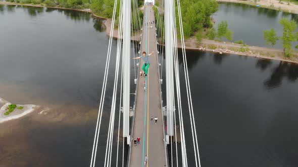 A Man Walks on a Rope Stretched Between the Supports of the Bridge at High Altitude. alt