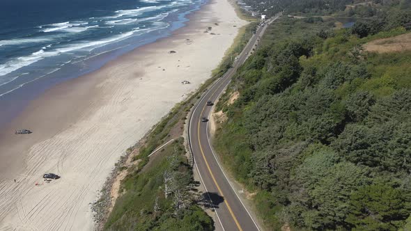 Aerial reveal of the scenic landscape of the Oregon Coast as cars drive on the scenic route 101. alt
