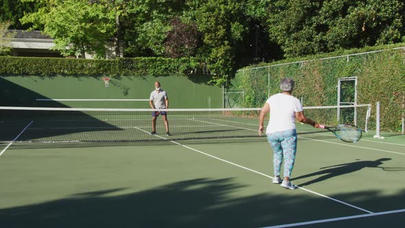 African american senior couple playing tennis on the tennis court on a bright sunny day alt