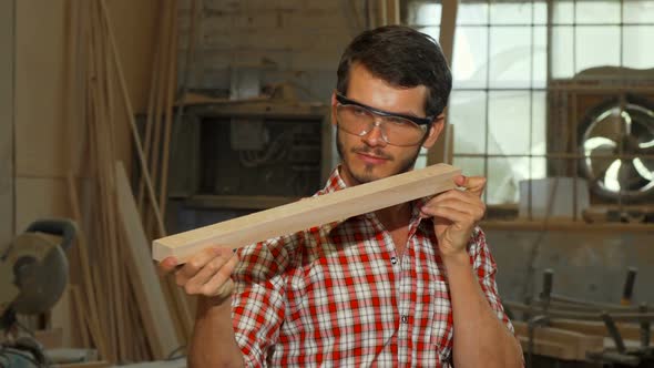 Bearded Carpenter Examining Wood Piece After Grinding It alt
