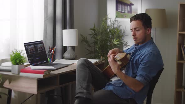 Young Designer Plays the Guitar While Resting From Work at Home in the Living Room alt