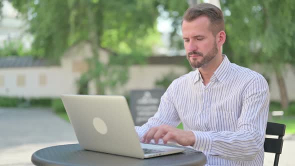 Middle Aged Man Working on Laptop in Outdoor Cafe alt