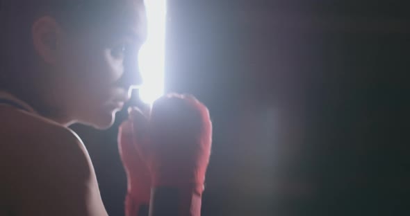 A Beautiful Woman Boxer Trains in a Dark Gym and Works Out Punches in Slow Motion. Side View alt
