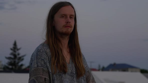 Young Man With Long Hair Meditating On City Roof alt