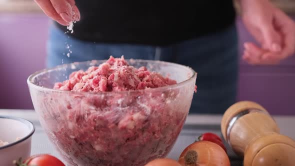 Adding Salt and Spices to Minced Meat with Onion and Spices in a Glass Bowl Making Cutlets alt