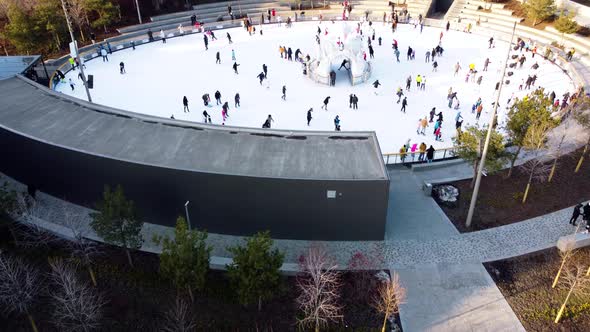 Many People are Skating on White Outdoor Ice Rink in City on Sunny Winter Day alt