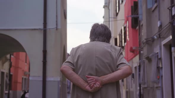 Elderly Stooped Woman Walks Down Narrow Street of Chioggia alt
