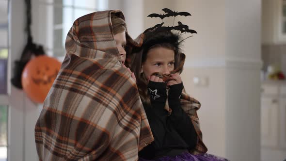 Scared Children Wrapped in Blanket Watching Horror Movie on Halloween Indoors alt