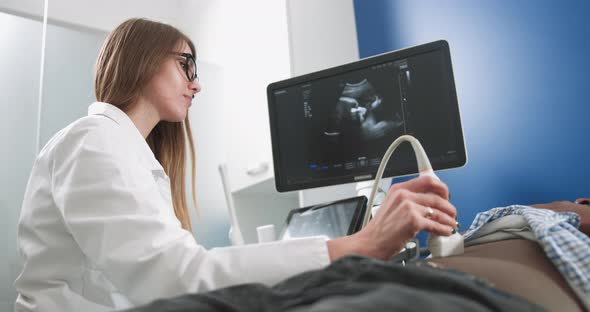 Focused Female Doctor Performs Ultrasound Examination of Internal Organs of Her alt