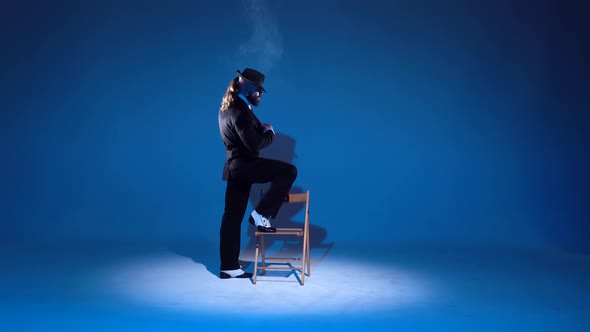 Elegant Man in a Black Hat Is Dancing an Erotic Dance. Spotlight on a Blue Background. alt