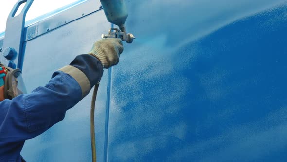 A Worker in Overalls and a Respirator Paints the Body of a Cargo Trailer or Metal Car in Blue