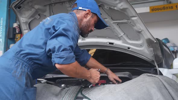 Young man is mechanic repairing engine of car in the garage, auto service. alt