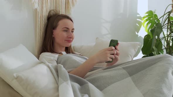Smiling Woman Using a Mobile Phone Was Lying on the Bed alt