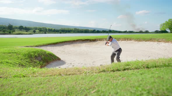 4K Asian senior man hitting golf ball from a bunker on golf course alt