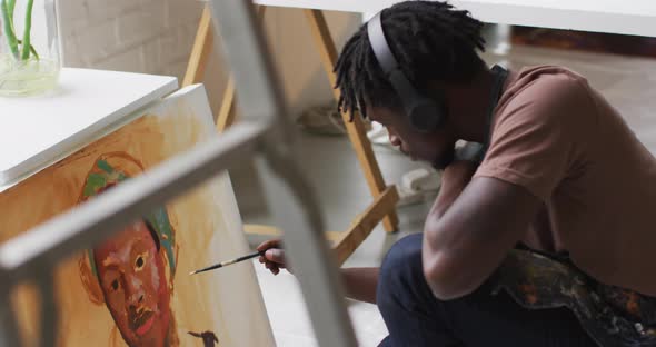 African american male artist wearing headphones painting on canvas at art studio alt