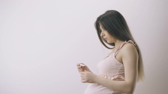 Pregnant Woman in Pink Dress Measures Temperature in Room alt