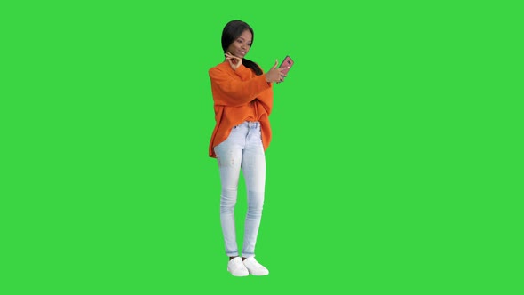 Smiling African American Woman in Bright Jumper Taking Selfie and Checking Her Phone on a Green alt