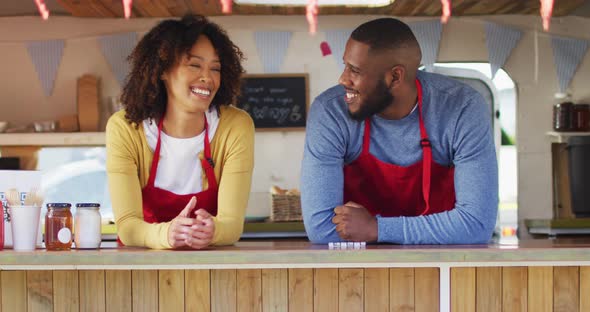 Portrait of african american couple wearing apron smiling while standing in the food truck alt