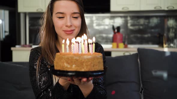A Young Caucasian Lady is Sitting at Home on the Sofa on Her Head Wearing a Birthday Cap and Holding alt