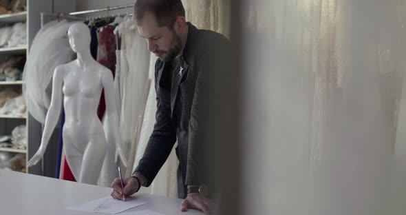 Male Designer Draws Sketch of Clothes in Atelier alt