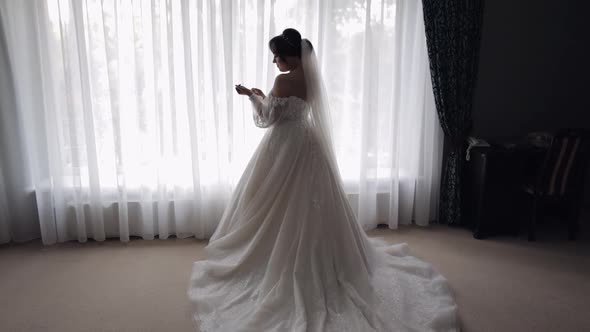 Smiling Bride in White Dress Staying at Home Bedroom Looking Sideways Wedding Preparations at Hotel alt