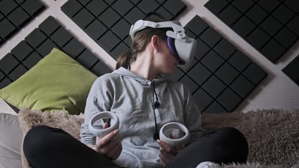 Young Woman in Virtual Reality Helmet Sitting on Sofa and Move Hands at Home alt