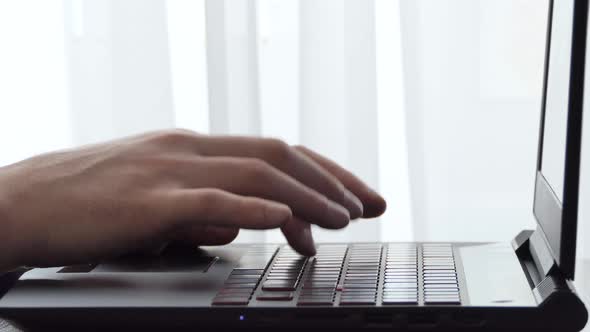 A Man Working with a Laptop on a Desktop Next to a Window alt