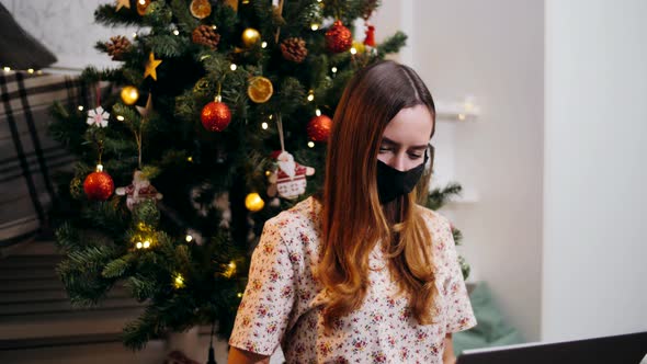 Cute girl in a respiratory mask works at a laptop on Christmas Eve