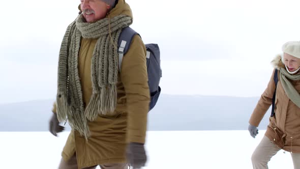 Adventurous Elderly Couple Waddling in Snow over Frozen Lake alt
