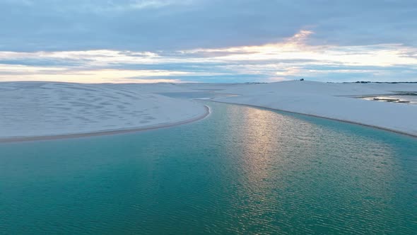 Drone Passes Over A Beautiful Blue Lagoon With White Sand Dunes At The End Of The Colorful Day