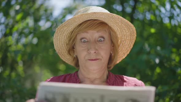 Dissatisfied Senior Woman Reading Newspaper Outdoors in Sunshine Throwing Away Paper in Slow Motion alt