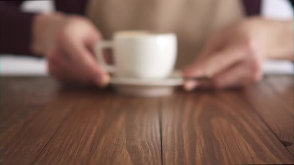 A Male Barista In A Beige Apron Serving A Cup Of Freshly Made Cappuccino. alt