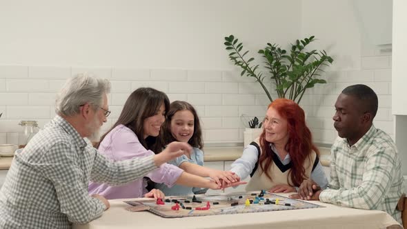 Multi Ethnic Family of Different Age Generations Play Board Game at Home Sitting at the Table alt