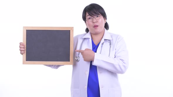 Happy Overweight Asian Woman Doctor Holding Blackboard and Giving Thumbs Up alt