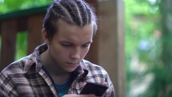 Teen Boy Sitting on Stairs at Home and Using App on His Mobile Phone alt