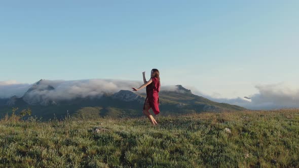 A Young Sexy Woman in a Red Dress is Performing a Shamanic Dance on the Top of a Hill in the Rays of alt